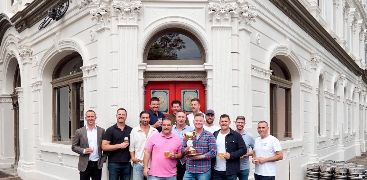 Group holding the Melbourne Cup outside the Doutta Galla Hotel's red doors